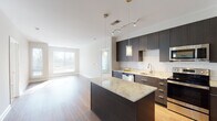 This single-floor residence showcases a contemporary design with high-quality finishes throughout. The kitchen is a standout feature, boasting dark espresso cabinetry that extends to the ceiling, a classic white subway tile backsplash, and light granite countertops on both the perimeter surfaces and a central island. Stainless steel appliances, including a refrigerator, range, microwave, and dishwasher, complete the well-appointed culinary space. Pendant lighting and a track rail system illuminate the kitchen and adjacent living area, which features warm hardwood flooring and large windows that invite generous natural light.

A carpeted bedroom with neutral tones opens through French doors to an outdoor area, providing a seamless indoor-outdoor connection. The bathrooms are finished with large-format tile flooring, floating dark-wood vanities, white countertops, and oversized mirrors. An in-unit stacked washer and dryer adds everyday convenience. A walk-in closet with wire shelving offers ample storage. The overall layout, visible through the 3D floor plan, presents a well-organized flow between living, sleeping, and utility spaces, all unified by a consistent modern aesthetic.