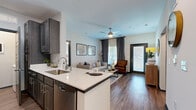 Located in Smyrna, Tennessee, this 2-bedroom, 2-bathroom single-story residence offers a thoughtfully designed open-concept layout with modern finishes throughout. The kitchen serves as a central hub, featuring dark espresso cabinetry, stainless steel appliances, a built-in sink, and a white quartz peninsula that flows seamlessly into the dining and living areas. The dining room accommodates a full-sized table and is brightened by a large window, while the living room offers warm wood-style flooring, a ceiling fan, and a glass door opening to a private exterior entrance with abundant natural light. The primary bedroom is a comfortable retreat with plush carpeting, a ceiling fan, and a dedicated window, while the second bedroom offers similar finishes. A well-appointed hallway connects the bedrooms to the two bathrooms, which feature dark cabinetry and white countertops consistent with the home's design language. A dedicated in-unit laundry room with a full-size washer adds everyday convenience. Neutral wall tones, bold dark-paneled interior doors, and cohesive design details tie each space together, creating a polished and functional home in the heart of Smyrna.