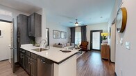 Located in Smyrna, Tennessee, this 2-bedroom, 2-bathroom single-story residence offers a thoughtfully designed open-concept layout with modern finishes throughout. The kitchen serves as a central hub, featuring dark espresso cabinetry, stainless steel appliances, a built-in sink, and a white quartz peninsula that flows seamlessly into the dining and living areas. The dining room accommodates a full-sized table and is brightened by a large window, while the living room offers warm wood-style flooring, a ceiling fan, and a glass door opening to a private exterior entrance with abundant natural light. The primary bedroom is a comfortable retreat with plush carpeting, a ceiling fan, and a dedicated window, while the second bedroom offers similar finishes. A well-appointed hallway connects the bedrooms to the two bathrooms, which feature dark cabinetry and white countertops consistent with the home's design language. A dedicated in-unit laundry room with a full-size washer adds everyday convenience. Neutral wall tones, bold dark-paneled interior doors, and cohesive design details tie each space together, creating a polished and functional home in the heart of Smyrna.