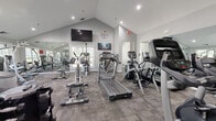Located at 79 Village Dr in Wethersfield, Connecticut, this single-story fitness center offers a comprehensive and well-organized exercise facility. The space is divided into two distinct areas: a fully equipped gym and a separate open studio room.

The main gym area features soaring vaulted ceilings that lend an open, airy feel to the space. The room is outfitted with a wide variety of cardio and strength equipment, including treadmills, elliptical trainers, stair climbers, stationary bikes, and Cybex cable machines. Full-length wall mirrors visually expand the space and support proper form during workouts. Recessed lighting and a wall-mounted television add comfort and convenience. Patterned carpet tile flooring covers the gym floor, and multiple windows allow natural light to filter in.

A connecting corridor leads to the studio space, which features large windows on multiple walls, flooding the room with natural light and offering views of the surrounding greenery. The studio is finished with neutral tile flooring and a full-wall mirror, making it well-suited for yoga, stretching, or group fitness classes. French doors connect the two areas, reinforcing a cohesive and functional layout throughout the facility.