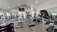 Located at 79 Village Dr in Wethersfield, Connecticut, this single-story fitness center offers a comprehensive and well-organized exercise facility. The space is divided into two distinct areas: a fully equipped gym and a separate open studio room.

The main gym area features soaring vaulted ceilings that lend an open, airy feel to the space. The room is outfitted with a wide variety of cardio and strength equipment, including treadmills, elliptical trainers, stair climbers, stationary bikes, and Cybex cable machines. Full-length wall mirrors visually expand the space and support proper form during workouts. Recessed lighting and a wall-mounted television add comfort and convenience. Patterned carpet tile flooring covers the gym floor, and multiple windows allow natural light to filter in.

A connecting corridor leads to the studio space, which features large windows on multiple walls, flooding the room with natural light and offering views of the surrounding greenery. The studio is finished with neutral tile flooring and a full-wall mirror, making it well-suited for yoga, stretching, or group fitness classes. French doors connect the two areas, reinforcing a cohesive and functional layout throughout the facility.