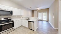 Located at 3555 Sweetwater Rd in Duluth, GA, this one-bedroom, one-bathroom unit offers a well-organized single-floor layout designed for comfortable everyday living. The open-concept kitchen, dining, and living area forms the heart of the home, featuring white cabinetry, light quartz-style countertops, a peninsula breakfast bar, and a full suite of stainless steel appliances including a refrigerator, range, microwave, and dishwasher. Light wood-style flooring runs throughout the main living areas, lending warmth and a clean, cohesive aesthetic. A ceiling fan in the living room and French doors leading to a private balcony bring in natural light and outdoor views. The bedroom is a comfortable, carpeted retreat with a window dressed in blinds, a ceiling fan, and access to a dedicated closet. The bathroom is finished with a white vanity, a large mirror, wood-style flooring, and accessibility-friendly grab bars. Additional practicalities include a utility room and in-unit laundry. Neutral warm-gray walls throughout create a calming, move-in-ready atmosphere suited to a variety of décor styles.