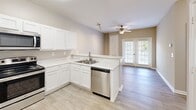Located at 3555 Sweetwater Rd in Duluth, GA, this one-bedroom, one-bathroom unit offers a well-organized single-floor layout designed for comfortable everyday living. The open-concept kitchen, dining, and living area forms the heart of the home, featuring white cabinetry, light quartz-style countertops, a peninsula breakfast bar, and a full suite of stainless steel appliances including a refrigerator, range, microwave, and dishwasher. Light wood-style flooring runs throughout the main living areas, lending warmth and a clean, cohesive aesthetic. A ceiling fan in the living room and French doors leading to a private balcony bring in natural light and outdoor views. The bedroom is a comfortable, carpeted retreat with a window dressed in blinds, a ceiling fan, and access to a dedicated closet. The bathroom is finished with a white vanity, a large mirror, wood-style flooring, and accessibility-friendly grab bars. Additional practicalities include a utility room and in-unit laundry. Neutral warm-gray walls throughout create a calming, move-in-ready atmosphere suited to a variety of décor styles.