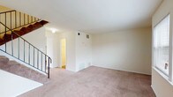 This two-story home in College Park, Georgia offers a practical and straightforward layout spread across two levels. The main level centers around a generously sized living area finished with plush carpet flooring and neutral cream-toned walls, creating a clean, understated backdrop. A staircase with a black metal railing connects the floors, adding a subtle structural detail to the space. The kitchen is equipped with white cabinetry offering ample storage, granite-patterned countertops, a double sink, and black appliances including an electric range, dishwasher, and a full-size refrigerator. Wood-look flooring runs throughout the kitchen, adding warmth and easy maintenance. A half bathroom on the main level features wood-look flooring, a compact white vanity with a mirror, and a towel bar. Upstairs, the primary bedroom is a spacious retreat with soft carpet, multiple windows that invite natural light and outdoor views, and access to a walk-in closet. An additional room on the upper level features wood-look plank flooring and clean walls. The full upstairs bathroom includes a shower-tub combination, white vanity, and a large mirror with overhead lighting.