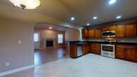 Located at 2403 S 15th Pl in Rogers, Arkansas, this two-story home offers a well-designed layout with distinct living spaces across both floors. The main level centers around an open-concept kitchen and living area connected by an arched passageway. The kitchen is equipped with stainless steel appliances—including a range, microwave, and dishwasher—rich wood cabinetry, and dark granite countertops, all set atop light tile flooring. A dedicated living room features a fireplace flanked by windows, while an adjacent area showcases impressively tall vaulted ceilings and wood-look tile flooring, adding a sense of grandeur. A half bath on the main level includes an ornate dark wood vanity with a granite top and decorative mirror. The staircase leads to the upper level, where carpeted rooms provide comfort underfoot. A generously sized loft or bonus room with built-in shelving offers flexible living space. The primary bedroom features vaulted ceilings, a ceiling fan, and a walk-in closet, while the en-suite bathroom includes a dual-sink vanity with granite countertops, tile flooring, and access to a walk-in closet with built-in shelving. Ceiling fans are present throughout the upper level, contributing to a comfortable and functional overall atmosphere.