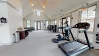 Located at Ashley Gardens in Charleston, SC, this fitness center is designed to support a comprehensive range of workout routines in a clean, well-lit environment. The facility is organized across two connected areas, each serving a distinct fitness purpose.

The main workout room features soaring vaulted ceilings and an abundance of natural light streaming through multiple large windows, creating an open and energizing atmosphere. Floor-to-ceiling mirrors line the walls, amplifying the sense of space. The room is outfitted with treadmills, elliptical machines, and a cable strength machine, all positioned on plush, light-colored carpeting. Barn-style doors with distinctive X-pattern detailing connect this space to an adjacent studio, while pendant and gooseneck barn lights add a refined architectural touch.

The adjoining studio room offers a more intimate setting for group or individual training. It is equipped with stationary cycling bikes, a rack of colorful dumbbells, exercise balls on a vertical storage rack, step platforms, kettlebells, medicine balls, and an adjustable weight bench. A window provides natural light and outdoor views of the surrounding greenery. Pendant lighting and a neutral color palette keep the space feeling fresh and functional. Together, both areas form a well-rounded fitness destination suited for cardio, strength training, and group exercise alike.
