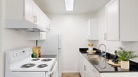 This single-floor residence offers a practical and cohesive layout encompassing a bedroom, bathroom, kitchen, dining room, closet, and entrance. The living and dining areas feature a neutral color palette with soft carpeted flooring and a warm tile transition near the dining space, which is accented by a classic chandelier overhead. The carpeted bedroom is a comfortable size, offering a window that brings in natural light and a clean, simple design with ample wall space. A dedicated closet provides convenient storage. The galley-style kitchen is efficiently designed with crisp white cabinetry, dark granite-style countertops, a stainless steel double sink, a skylight overhead, and white appliances including an electric range and refrigerator — maximizing both function and brightness. The bathroom continues the cohesive aesthetic with matching white cabinetry, dark countertops, tile flooring, a large vanity mirror, and a full tub-shower combination. Throughout the residence, white walls and consistent finishes create a bright, clean atmosphere. The thoughtful floor plan ensures every space is purposefully utilized, making this a well-rounded and comfortable single-level home.