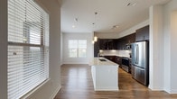 Located at 18610 Tuscany Stone in San Antonio, TX, this thoughtfully designed single-floor residence offers a clean, contemporary aesthetic throughout. Entry is made through a sleek paneled white door that opens onto hardwood-style flooring, setting the tone for the modern finishes found across the unit.

The heart of the home is an open-concept kitchen and living area bathed in natural light from multiple large windows with horizontal blinds. The kitchen is a standout, featuring rich dark cabinetry with glass-front upper panels, a white granite island with an undermount sink, stainless steel appliances including a French door refrigerator and range, white subway tile backsplash, and stylish pendant lighting overhead. Track lighting above the cooking area adds both function and visual interest.

A hallway with a double-door closet provides convenient storage and connects the main living area to the private quarters. The bedrooms feature plush neutral carpet and generous windows that invite natural light and offer views of the surrounding landscape. Ceiling fans are present in the bedrooms for added comfort.

The bathrooms are finished with large-format tile flooring, dark vanity cabinetry, granite countertops, and framed mirrors. The primary bathroom includes a walk-in tiled shower and direct access to a spacious walk-in closet, while the secondary bath offers a clean, functional layout with ample storage.