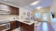 Located in Suwanee, GA, this single-story, one-bedroom, two-bathroom residence offers a thoughtfully designed open-concept layout that maximizes its comfortable footprint. The kitchen is a standout feature, showcasing rich dark-wood cabinetry, light quartz countertops, stainless steel appliances including a refrigerator, range, microwave, and dishwasher, and a peninsula with a double sink that overlooks the living area — ideal for both cooking and entertaining. Hardwood flooring flows through the kitchen and living room, where natural light pours in through multiple windows and a glass exterior door. A wall-mounted mini-split HVAC system provides efficient climate control throughout. The living room offers a relaxed, open ambiance with direct outdoor access. The generously sized primary bedroom features carpeted flooring, a window with outdoor views, a built-in closet, and its own mini-split unit. It connects directly to a private bathroom equipped with a large, fully tiled roll-in shower with stainless steel grab bars — reflecting thoughtful accessibility design. A second bathroom mirrors this attention to accessibility. A dedicated laundry area completes this well-organized, single-level home.