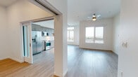 This single-floor residence showcases a clean, contemporary design throughout, with light-toned hardwood flooring and crisp white walls creating a bright, cohesive aesthetic. The entry foyer provides a welcoming introduction to the space, complete with a programmable thermostat and a secure front door. The open-concept living and kitchen area forms the heart of the unit, bathed in natural light from large windows that frame expansive city views. A ceiling fan with a light fixture anchors the living area, while track lighting over the kitchen provides focused illumination. The kitchen is well-appointed with taupe flat-front cabinetry, white subway tile backsplash, light quartz countertops, and a full suite of stainless steel appliances including a side-by-side refrigerator, range, microwave, and dishwasher. The bedrooms offer generous proportions, with hardwood flooring and ample closet space, including both sliding and louvered-door closets. Two bathrooms serve the unit: one features a walk-in glass-enclosed shower with built-in shelving, while the second includes a soaking tub with tiled surround. Both bathrooms maintain the unit's clean, modern aesthetic with contemporary vanities and wood-tone flooring.