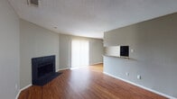 This single-floor residence offers a well-organized layout with a variety of functional spaces designed for comfortable everyday living. The open living area serves as the heart of the home, featuring warm wood-look flooring, a black-surround fireplace, and a sliding glass door fitted with vertical blinds that allows natural light to fill the room. A half-wall pass-through connects the living area to the kitchen, adding an open, airy feel to the space.

The galley-style kitchen is equipped with warm wood cabinetry extending to the ceiling for ample storage, black appliances including a full-size refrigerator and range, a built-in sink, and light-toned countertops. The textured ceiling continues throughout the kitchen, consistent with the rest of the home's interior finish.

The bedrooms feature plush carpeting and neutral wall tones, offering a quiet and comfortable retreat. One bedroom benefits from a window with blinds providing natural light, and connects directly to the bathroom. The bathroom includes rich wood cabinetry overhead, a granite-style countertop vanity, a large mirror, and wood-look flooring that complements the rest of the home.

A hallway with hardwood-style flooring links the various rooms together, providing a cohesive flow throughout the single-story layout. Neutral gray walls and textured ceilings are consistent design elements found throughout the residence.