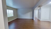 This single-floor, one-bedroom, one-bathroom unit offers a thoughtfully organized layout that maximizes its compact footprint. The combined kitchen and living area forms the heart of the space, featuring light hardwood-style flooring that extends throughout the main areas, creating a cohesive and clean aesthetic. The kitchen is equipped with gray cabinetry, a stainless steel refrigerator, a built-in sink with under-counter storage, and light countertops — providing a practical and modern workspace. The open layout allows the kitchen to flow naturally into the living area, which benefits from a window that admits natural light and connects to the rest of the unit through a defined hallway.

The bedroom is a comfortable, well-proportioned room finished with plush carpet flooring and features a window fitted with white horizontal blinds, allowing for natural light and privacy control. Neutral gray-white walls throughout the unit contribute to a calm, versatile atmosphere.

The bathroom is finished with white subway tile surrounding a full tub-shower combination, complemented by gray cabinetry above and a vanity with ample storage. A dedicated entrance and hallway provide a clear transition between rooms, contributing to the unit's organized and functional flow.