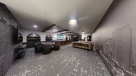 Located at 18807 8th Ave NE in Shoreline, Washington, this single-floor entertainment lounge is a thoughtfully designed social space that blends modern aesthetics with upscale amenities. The open-plan layout accommodates multiple distinct activity zones, all unified by a cohesive dark, urban design palette.

A standout feature is the dramatic floor-to-ceiling city skyline mural that spans an entire wall, creating a sophisticated metropolitan ambiance throughout the space. Exposed dark wood ceiling beams add architectural character and warmth, contrasting beautifully with the light-toned ceiling and recessed lighting above.

The full wet bar runs along one side of the room, featuring a dark stone countertop, warm wood cabinetry, and elegant arched alcoves with built-in shelving for spirits and glassware. High-back bar stools with gold-accented legs line the counter, while a separate high-top table with seating provides additional gathering space nearby.

A large flat-screen television is mounted on a textured brick accent wall, creating a dedicated media viewing area. Adjacent to it, a poker or game table surrounded by curved lounge chairs offers a dedicated space for recreational play.

The lounge seating area features comfortable sofas arranged around a coffee table, ideal for casual conversation. Patterned carpeting with a terrazzo-inspired design ties the entire space together, completing this polished and versatile entertainment venue.