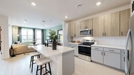 This well-appointed one-bedroom, one-bathroom residence in Denver, Colorado offers a thoughtfully designed open-concept layout that maximizes every square foot. Light wood-tone flooring flows throughout, lending warmth and visual continuity across the space.

The kitchen is a standout feature, showcasing a two-tone cabinet design that pairs natural wood uppers with sleek gray lowers, complemented by white quartz countertops and a matching waterfall island with bar seating. Stainless steel appliances — including a refrigerator, electric range, and built-in microwave — complete this highly functional culinary space. The kitchen opens seamlessly into the living area, which is bathed in natural light and features access to a private balcony offering views of the Denver skyline.

The bedroom is a cozy retreat with soft carpeting, a ceiling fan, warm accent wall tones, and a window that brings in natural light and city views. The full bathroom is finished with a wide vanity featuring gray cabinetry, a white quartz countertop, matte black hardware, a large mirror, and a tiled walk-in shower. An in-unit laundry area accommodates full-size washer and dryer units, adding everyday convenience to this modern Denver residence.
