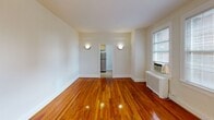 Located at 829 Quincy St NW in Washington, DC's Petworth neighborhood, this second-floor apartment offers a well-organized single-level layout with classic character and practical finishes throughout. The living area is a standout space, showcasing richly toned, polished hardwood floors that extend through the main living spaces and bedroom. Soft wall sconces provide warm ambient lighting, while multiple windows fitted with blinds allow natural light to fill the rooms and offer views of the surrounding neighborhood. The bedroom mirrors the living area's aesthetic with the same gleaming hardwood floors, a ceiling light fixture, and a window-mounted air conditioning unit alongside a radiator, ensuring year-round comfort. The kitchen is equipped with light wood cabinetry offering ample storage, a dark stone-style countertop, a stainless steel refrigerator, and a gas range, all set on durable tile flooring. The bathroom features a full-size soaking tub and shower combination with clean white tile surround and chrome fixtures, along with overhead cabinetry for additional storage. The layout flows efficiently from room to room, making practical use of the available space while maintaining a cohesive, bright, and neutral aesthetic throughout.
