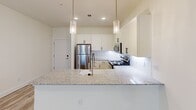This single-floor unit offers three bedrooms, one bathroom, and a thoughtfully designed open-concept kitchen and living area. The living room features light wood-look luxury vinyl plank flooring, neutral cream-toned walls, and windows with blinds that allow natural light to fill the space. A private entry door is accessible directly from the living area.

The kitchen is a standout feature, showcasing white shaker-style cabinetry, granite countertops, a tile backsplash, stainless steel appliances, and a peninsula with pendant lighting — ideal for both meal preparation and casual dining.

The primary bedroom is generously proportioned, featuring soft carpeting, a ceiling fan with lighting, a walk-in closet, and direct access to the bathroom. The two additional bedrooms also feature carpet flooring and ceiling-mounted light fixtures; one includes a closet and a window with natural light views.

The bathroom is clean and modern, with a granite-topped vanity, white cabinetry, a tub-shower combination, and wood-look flooring. Throughout the unit, a consistent neutral palette and contemporary finishes create a cohesive, move-in-ready environment.