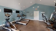 Located at 3009 Crossfork Dr in Wilmington, Delaware, this fitness center is a well-appointed, single-floor facility designed to support a comprehensive workout routine. The space is defined by striking vaulted ceilings that rise to a central peak, creating an open and airy atmosphere enhanced by recessed lighting and natural light flowing in through multiple windows with neutral blinds.

The interior is finished with calming teal-blue walls and durable dark flooring suited for high-traffic exercise use. The layout is thoughtfully organized into distinct functional zones. The cardio area features multiple treadmills and elliptical machines, each positioned in front of wall-mounted flat-screen televisions, making for an engaging workout experience. A motivational wall decal reading "Everyday is a good day to work out" adds an energizing touch to the space.

The strength training zone is equipped with a multi-station cable machine, a full dumbbell rack with a dedicated weight bench, and a stability ball for functional fitness. A rowing machine rounds out the equipment offerings. Additional amenities include a wall-mounted fan for ventilation, a wall clock, and informational postings. Two entry/exit doors provide convenient access. Overall, the space delivers a clean, functional, and well-maintained environment for fitness enthusiasts.