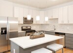 Located at 20 E 19th St in Bayonne, NJ, this single-floor residence offers a thoughtfully designed layout with modern finishes throughout. The kitchen serves as a standout feature, showcasing a two-tone cabinet scheme with white upper cabinets and gray lower cabinets, complemented by a classic subway tile backsplash, quartz countertops, and a full suite of stainless steel appliances including a gas range, built-in microwave, dishwasher, and French door refrigerator. A central island with pendant lighting provides additional prep space and casual seating.

The living area features hardwood flooring, neutral walls, and large windows that allow natural light to fill the room. Multiple bedrooms are finished with plush carpeting, generous windows, and closet storage. The primary bedroom includes a walk-in closet, adding practical functionality.

Two bathrooms serve the residence. The first features large-format tile flooring, a gray vanity with a white countertop, a tub-shower combination, and a wide mirror with contemporary lighting. The second bathroom offers dark tile flooring, a white vanity, and a walk-in shower. Together, these spaces reflect a clean, modern aesthetic consistent throughout the home.