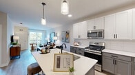 This well-appointed one-bedroom, one-bathroom residence at 250 McHenry Road in Buffalo Grove, Illinois offers a thoughtfully designed open-concept layout across a single floor. The heart of the home is a stylish, contemporary kitchen featuring two-tone cabinetry — crisp white upper cabinets paired with gray lower cabinets — set against a classic subway tile backsplash. Stainless steel appliances, a gas range, and a large center island with seating make this kitchen as functional as it is visually striking. Pendant lighting above the island adds a refined touch. The kitchen flows seamlessly into a combined dining and living area bathed in natural light, with a sliding glass door opening to a private balcony that offers pleasant outdoor views. The living area provides a welcoming, open ambiance with light wood-style flooring throughout. The spacious primary bedroom features plush carpeting, large windows that invite abundant natural light, and ample closet space — with three closets total throughout the residence. The bathroom is finished with a gray vanity, framed mirror, and warm wood-tone flooring, consistent with the home's modern aesthetic. A dedicated laundry area and a welcoming entrance complete this efficiently designed and elegantly finished home.