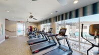 Located at 356 Lake Murray Boulevard in Irmo, South Carolina, this well-appointed fitness center offers a dedicated exercise space designed to support an active lifestyle. The single-floor layout makes efficient use of its footprint, accommodating a comprehensive selection of cardio equipment including multiple Star Trac treadmills, elliptical trainers, and stationary cycling bikes — all arranged to promote an open, accessible workout environment.

Large floor-to-ceiling windows line one side of the room, flooding the space with abundant natural light and providing direct views of an outdoor pool and pergola area, creating an energizing atmosphere during workouts. Striped valances add a decorative touch to the windows while softening the brightness. Recessed lighting and multiple ceiling fans are installed throughout, ensuring consistent illumination and comfortable airflow.

The neutral-toned carpet and warm beige walls give the room a clean, modern aesthetic, complemented by a curated selection of colorful, large-format artwork displayed on the walls, adding vibrancy and character. A glass-paneled door connects to an adjacent stairwell and exterior access, enhancing the room's connectivity. The overall ambiance is bright, functional, and inviting — well-suited for residents seeking a convenient, community fitness facility.