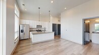 This thoughtfully designed one-bedroom, one-bathroom residence in Carmel, Indiana offers a clean, contemporary aesthetic throughout. The open-concept layout is anchored by a stunning kitchen featuring a large center island with quartz countertops, a black matte faucet, and a full suite of stainless steel appliances including a refrigerator, range, microwave, and dishwasher. Crisp white shaker cabinetry extends to the ceiling, maximizing storage, while a classic subway tile backsplash and pendant lighting add refined detail. Large windows flood the kitchen and living areas with abundant natural light. Light-toned hardwood flooring flows throughout the main living spaces, complementing the bright, neutral palette and soaring ceilings that enhance the sense of openness. The spacious bedroom is finished with plush carpet, tall windows offering outdoor views, and direct access to a private balcony. The full bathroom is elegantly appointed with a dual-sink vanity, quartz countertop, white cabinetry, matte black hardware, and a glass-enclosed walk-in shower. A dedicated closet provides practical storage. The overall ambiance is modern, airy, and move-in ready, reflecting high-quality finishes throughout.