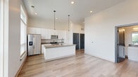 This thoughtfully designed one-bedroom, one-bathroom residence in Carmel, Indiana offers a clean, contemporary aesthetic throughout. The open-concept layout is anchored by a stunning kitchen featuring a large center island with quartz countertops, a black matte faucet, and a full suite of stainless steel appliances including a refrigerator, range, microwave, and dishwasher. Crisp white shaker cabinetry extends to the ceiling, maximizing storage, while a classic subway tile backsplash and pendant lighting add refined detail. Large windows flood the kitchen and living areas with abundant natural light. Light-toned hardwood flooring flows throughout the main living spaces, complementing the bright, neutral palette and soaring ceilings that enhance the sense of openness. The spacious bedroom is finished with plush carpet, tall windows offering outdoor views, and direct access to a private balcony. The full bathroom is elegantly appointed with a dual-sink vanity, quartz countertop, white cabinetry, matte black hardware, and a glass-enclosed walk-in shower. A dedicated closet provides practical storage. The overall ambiance is modern, airy, and move-in ready, reflecting high-quality finishes throughout.