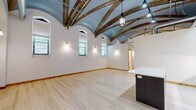 Located at 4611 S Ellis Ave in Chicago's Woodlawn neighborhood, this one-bedroom, two-bathroom unit is a standout example of adaptive reuse design. The space is defined by its dramatic vaulted, arched ceilings with ornate exposed ironwork and industrial ductwork, lending a loft-like grandeur that sets it apart from conventional residences. Light hardwood flooring flows throughout, complementing the bright, white-painted walls and warm wood trim accents on doors and baseboards.

The open living area is generously proportioned, bathed in natural light from a row of tall, arched windows that reinforce the architectural character of the space. The modern kitchen features sleek two-tone cabinetry, quartz countertops, a tile backsplash, stainless steel appliances including a gas range and dishwasher, and a substantial center island—ideal for both cooking and entertaining.

The bedroom offers a clean, serene retreat with wall sconce lighting and a window providing natural light and outdoor views. Both bathrooms are finished in crisp white tile; one includes a soaking tub and glass shower enclosure, while the other features a pedestal sink and a wood-framed mirror, both exuding a clean, minimalist aesthetic. A connecting hallway ties the layout together efficiently. This unit delivers a compelling blend of historic architectural detail and contemporary finishes.