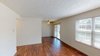This single-story space is designed with a functional, open layout that connects its primary living areas seamlessly. The main living room is a generously sized, light-filled area featuring rich, dark hardwood-style flooring that runs throughout most of the unit. Two windows, including a large sliding glass door, allow abundant natural light to pour in while providing outdoor access. A ceiling fan with a built-in light fixture adds both comfort and practicality to the space. Textured ceilings are present throughout, adding subtle visual character.

The galley-style kitchen is efficiently arranged with rich, dark wood cabinetry lining both sides, dark granite-style countertops, a double stainless steel sink, and black appliances including a refrigerator and dishwasher. A hallway leads from the kitchen toward additional rooms, including a dedicated laundry area equipped with a full-size washer and dryer.

The bedroom features plush wall-to-wall carpeting and a sizeable window offering outside views, creating a comfortable and quiet retreat. An additional room with hardwood-style flooring provides flexible use as a secondary bedroom or office. The neutral color palette throughout the space creates a clean, cohesive aesthetic well-suited for a variety of décor styles.