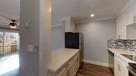This single-floor residence offers a thoughtfully designed layout with a blend of modern updates and comfortable living spaces. The galley-style kitchen is a standout feature, showcasing white shaker cabinetry crowned with elegant molding, quartz countertops, a mosaic tile backsplash in grey and white tones, and a full suite of stainless steel appliances including a refrigerator, range, dishwasher, and over-the-range microwave. Warm hardwood-style flooring runs throughout the kitchen and connects seamlessly to adjacent areas. The bedrooms are generously sized, bathed in natural light through wide windows that offer views of surrounding greenery. Each room features soft wall-to-wall carpeting, crown molding, and ceiling fans with integrated lighting, contributing to a comfortable and airy atmosphere. The bathrooms are well-appointed with white vanity cabinetry, quartz countertops, brushed gold fixtures, a mosaic tile backsplash above the vanity, and a tub-shower combination enclosed by sliding glass doors. Dark hardwood-style flooring in the bathrooms adds a refined contrast to the light finishes. Crown molding is consistent throughout the unit, lending a cohesive and polished character to the entire space.