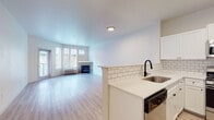 This single-floor residence offers a thoughtfully designed layout that balances open communal spaces with comfortable private areas. The open-concept living and dining area is anchored by a fireplace and bathed in natural light from a bank of windows, creating a welcoming atmosphere. Light-toned hardwood-style flooring flows throughout the main living area, reinforcing the clean, contemporary feel of the space.

The kitchen is well-appointed with white shaker cabinetry, a classic subway tile backsplash, light stone countertops, and a full suite of stainless steel appliances, including a gas range, over-the-range microwave, and a full-size refrigerator. A raised peninsula with a stainless steel sink separates the kitchen from the living area, making it ideal for both cooking and entertaining.

The bedrooms are carpeted for comfort and feature neutral walls, ample closet space with built-in shelving, and access to natural light. One bedroom opens directly onto a private balcony through a sliding glass door, offering outdoor views of surrounding greenery. The bathrooms are finished with light wood-look flooring, white cabinetry with dark hardware accents, and a tiled shower-tub combination, maintaining the home's consistent modern aesthetic throughout.