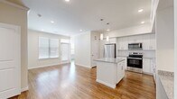 This thoughtfully designed 2-bedroom, 2-bathroom single-story residence offers a functional and modern layout with consistent hardwood flooring flowing throughout every room. The open-concept kitchen serves as the centerpiece of the living area, featuring white shaker cabinetry extending to the ceiling, granite countertops, a central island, stainless steel appliances including a refrigerator, range, microwave, and dishwasher, and elegant pendant lighting overhead. A built-in desk nook with matching granite countertop and open shelving adds a practical workspace adjacent to the kitchen. Crown molding and recessed lighting enhance the clean, polished aesthetic of the main living area, which receives generous natural light through large windows. Both bedrooms are bright and comfortable, each equipped with a ceiling fan and natural light from windows with blinds. The primary bedroom connects to a well-sized walk-in closet with multi-tier shelving and a private en-suite bathroom featuring a granite vanity, white cabinetry, and a glass-enclosed shower. The second bathroom offers a full tub-shower combo, granite vanity, and white cabinetry. Two closets provide ample storage throughout the residence.