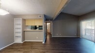 This single-floor unit offers a well-organized layout with a cohesive design throughout. The living area is a standout space, featuring vaulted ceilings with exposed beams, dark hardwood-style flooring, and a brick fireplace that serves as a focal point. A sliding glass door allows natural light to pour in while providing outdoor access. The open-concept design connects the living area to the kitchen, which is separated by a peninsula counter ideal for casual dining or meal prep. The kitchen is well-equipped with light wood cabinetry extending to the ceiling, a built-in skylight, black appliances including a refrigerator, range, microwave, and dishwasher, along with a single-basin sink. A hallway leads to the private areas of the unit, including a bedroom that features two windows fitted with white blinds, a ceiling fan with light fixture, and the same dark hardwood-style flooring found throughout. The bedroom also benefits from a spacious walk-in closet with dual shelving rails on both sides. The bathroom includes a tiled tub and shower combination with a built-in shelf niche and chrome fixtures. Textured ceilings are consistent throughout, adding a classic architectural touch to the space.