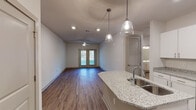 Located at 6318 Litchford Rd in Raleigh, NC, this single-floor unit offers a thoughtfully designed layout with contemporary finishes throughout. The open-concept kitchen and living area serves as the heart of the space, where a curved granite-topped island with an undermount sink anchors the kitchen. Pendant lights hang above the island, complementing the recessed lighting overhead. The kitchen is well-appointed with crisp white cabinetry extending to the ceiling, light granite countertops, and a full suite of stainless steel appliances, including a refrigerator, range, and microwave. Wood-style flooring runs consistently throughout the unit, lending a warm, cohesive aesthetic. The living area is generously sized, featuring a ceiling fan and French doors that invite natural light and provide outdoor access. The bedrooms are comfortably proportioned, each with wood-style flooring and ceiling fans or natural light from windows with blinds. Multiple closeted doors are visible off the hallway. The bathrooms are clean and functional, featuring white vanities, large mirrors, and wood-style flooring, with one bathroom including a glass-enclosed walk-in shower. Overall, the unit presents a fresh, modern aesthetic with consistent finishes.