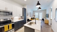 This thoughtfully designed one-bedroom, two-bathroom residence offers a smart, efficient layout across a single floor. The open-concept kitchen serves as a centerpiece, showcasing striking two-tone cabinetry with navy lower cabinets, white upper cabinets, and gold-toned hardware. White quartz countertops extend across the workspace and onto a central island with an integrated sink, illuminated by a pair of industrial-style pendant lights. Stainless steel appliances, including a French door refrigerator, electric range, and over-the-range microwave, complete the well-equipped kitchen. Wood-look herringbone-patterned flooring flows seamlessly from the kitchen into the living area, which is bathed in natural light from floor-to-ceiling glass doors leading to the outdoors. The bedroom offers a comfortable, well-sized retreat with large windows, plush carpeting, and ample wall space. Two full bathrooms provide added convenience, and an in-unit washer area with shelving adds practical functionality. Throughout the residence, crisp white walls and carefully considered finishes create a bright, contemporary ambiance that balances style with everyday livability.
