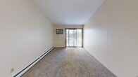 This single-floor, 2-bedroom, 2-bathroom unit offers a practical and straightforward layout across a comfortable footprint. The living room is carpeted and features a sliding glass door with vertical blinds that allows natural light to flow in, complemented by a wall-mounted AC unit and baseboard heating. Adjacent to the living room, the kitchen is equipped with wood-look laminate flooring, white cabinetry with wood-tone trim, a double sink, a white refrigerator, a white range, and a black dishwasher — providing ample functionality for everyday use. A central hallway with carpet flooring and textured walls connects the main living areas to the bedrooms and bathrooms, with wood-panel doors adding a warm touch throughout. The spacious primary bedroom features carpet flooring, a ceiling fan with light fixture, a baseboard heater, and a window with vertical blinds. The second bedroom is also carpeted and includes a closet with wood-panel bifold doors. Both bathrooms are clean and utilitarian: one features a full tub/shower combo, while the other offers a walk-in shower, both with tile flooring. Textured ceilings are consistent throughout the unit, lending a cohesive aesthetic to the overall space.