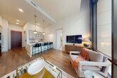 This contemporary single-floor urban residence delivers a refined living experience defined by clean lines, high-end finishes, and abundant natural light. The open-concept living area is anchored by dramatic floor-to-ceiling windows that frame sweeping city views and flood the interior with daylight. Dark accent walls and bold artwork create a striking contrast against the light hardwood flooring that flows throughout the main living spaces.

The gourmet kitchen is appointed with gray shaker cabinetry, a white quartz waterfall island with bar seating, a professional stainless steel gas range with a wall-mounted hood, and a French door refrigerator. Pendant lighting above the island adds a warm, functional accent to the culinary space.

The bedrooms are generously proportioned, each featuring large floor-to-ceiling windows offering urban vistas and plush carpeting for comfort. The primary bedroom is complemented by a well-appointed en-suite bathroom featuring a walk-in shower, dual vanity with dark countertops, and direct access to an organized walk-in closet.

The bathroom is finished with light wood-look tile flooring and white cabinetry, providing a clean and functional aesthetic. Throughout the residence, thoughtful architectural details and premium materials come together to create an elegant, comfortable, and distinctly urban living environment.