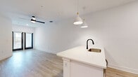 This well-designed 1-bedroom, 1-bathroom unit offers a thoughtfully arranged single-floor layout that maximizes every square foot. The open-concept living and kitchen area sets a bright, modern tone, anchored by light-toned luxury vinyl plank flooring that flows seamlessly throughout the entire space. The kitchen is a standout feature, showcasing crisp white shaker cabinetry with matte black hardware, a white quartz peninsula with an undermount sink and black gooseneck faucet, stainless steel appliances including a refrigerator, range, and over-the-range microwave, and a classic white tile backsplash. Stylish pendant lights hang above the peninsula, complementing the open living area beyond, which is equipped with a ceiling fan. The bedroom is a comfortable, well-proportioned retreat filled with natural light from large windows and outfitted with its own ceiling fan. It connects to a generously sized walk-in closet with full wire shelving systems on all walls, providing excellent storage capacity. The bathroom features a clean, all-white tub and shower combination with matte black fixtures, including a rain-style showerhead, paired with a white vanity and wood-look flooring. The overall aesthetic is fresh, modern, and move-in ready.