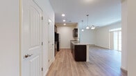 This single-floor residence offers a thoughtfully designed open-concept layout that seamlessly connects the kitchen, dining, and living areas. The kitchen is a standout feature, showcasing rich dark-espresso cabinetry paired with granite countertops, a center island with a built-in sink, and a full suite of stainless steel appliances including a refrigerator, range, microwave, and dishwasher. Light wood-style flooring runs throughout the main living areas, lending warmth and continuity to the space. The living area is bright and inviting, illuminated by recessed lighting and a ceiling fan with integrated light fixture. A set of sliding glass doors with transom windows above floods the room with natural light and opens to a private outdoor balcony with views of surrounding greenery. The bedrooms are carpeted for comfort and feature generous closet space, including a double-door closet in the primary bedroom. Additional doors off the main corridor provide access to utility and storage areas. The layout is efficient and functional, with clean white walls and neutral tones throughout that create a fresh, move-in-ready atmosphere well-suited for everyday living.
