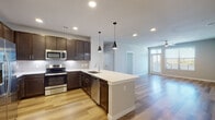 This single-floor residence offers a thoughtfully designed open-concept layout that seamlessly connects the kitchen and living area. The kitchen is a standout feature, showcasing rich dark-brown cabinetry with sleek hardware, a classic white subway tile backsplash, and a full suite of stainless steel appliances including a French door refrigerator, range, microwave, and dishwasher. A generous island with a crisp white countertop and an undermount sink anchors the space, complemented by stylish pendant lighting overhead. Light-toned hardwood-style flooring runs throughout the main living areas, enhancing the bright, open feel. The living area extends naturally from the kitchen, complete with a ceiling fan and access to natural light through exterior windows. The bedrooms are finished with plush neutral carpeting, ceiling fans, and windows with blinds that bring in comfortable natural light and outdoor views. Two bathrooms serve the residence, each featuring dark cabinetry with white countertops. One bathroom offers a tub-shower combination with white subway tile surround, while the other provides a longer vanity and window for added brightness. Recessed lighting throughout and a neutral, contemporary color palette give the entire space a clean, modern ambiance.