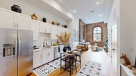 Located at 179 Chelsea Ave in Long Branch, NJ, this 1-bedroom, 1-bathroom unit masterfully blends historic architectural character with modern finishes. The space is defined by dramatic exposed brick walls and striking arched windows that soar toward high ceilings, flooding the interior with natural light and lending an unmistakable industrial-chic aesthetic.

The open kitchen is thoughtfully appointed with crisp white shaker cabinetry, marble-look countertops, stainless steel appliances including a refrigerator, range, microwave, and dishwasher, and a sleek black-accented sink. A bar-height dining table anchors the kitchen area, making it ideal for casual dining.

The living room continues the dramatic brick backdrop, with tall arched windows framing outdoor views and creating an airy, loft-like atmosphere. Warm hardwood floors run throughout the main living areas, complementing the rich tones of the exposed masonry.

The bedroom offers a serene retreat, featuring soaring ceilings, an arched brick-framed window, and direct access to a dedicated closet with built-in hanging storage. Soft carpeting adds comfort underfoot.

The bathroom is clean and modern, with large-format tile flooring, a white vanity with marble countertop, an illuminated mirror, and a shower stall. Every detail reflects a carefully considered, contemporary design sensibility.