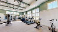 Located at Lakeview Ridge Circle in Apopka, Florida, this expansive single-floor fitness center is thoughtfully designed to support a comprehensive workout experience. The facility features soaring ceilings accented by exposed beam detailing and large ceiling fans, contributing to an open, airy atmosphere throughout the space. Walls are finished in a two-tone scheme of sage green above white wainscoting, lending the interior a fresh, modern aesthetic.

Large multi-pane windows line the perimeter, flooding the facility with generous natural light and offering pleasant outdoor views of the surrounding Florida landscape. The main workout floor is finished with light, neutral tile in a herringbone pattern, providing a clean and durable surface underfoot.

The cardio zone is well-stocked with a full lineup of TRUE-brand treadmills, ellipticals, stair climbers, and cycling bikes. An extensive free weights area features a full dumbbell rack backed by floor-to-ceiling mirrors, accompanied by adjustable benches and a wall-mounted television. Functional training is supported by a dedicated zone equipped with kettlebells, medicine balls, battle ropes, resistance equipment, and rowing machines. Additional cable and strength machines are distributed throughout the space. French doors provide convenient entry and exit, completing this bright and fully outfitted fitness facility.