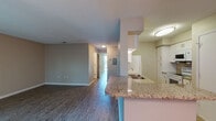 Located at 5779 Summerside Ln in Sarasota, Florida, this single-story residence offers a well-organized layout with a consistent, neutral color palette and wood-style flooring throughout. The open living area is a standout feature, bathed in natural light courtesy of a sliding glass door that leads to a private balcony overlooking a verdant, tree-lined backdrop — bringing a sense of the outdoors inside. Vertical blinds provide adjustable light control and privacy.

The kitchen is thoughtfully designed with an open-concept peninsula topped in granite, offering both workspace and a casual bar-style seating area. White cabinetry, a built-in microwave, electric range, refrigerator, and a stainless steel sink complete the functional kitchen setup. The peninsula opens directly to the main living and dining area, promoting a connected, social atmosphere.

The bedrooms are comfortably sized, each featuring wood-style flooring, neutral taupe walls, and mirrored sliding closet doors that enhance the sense of space. The layout flows naturally from the entry, past the kitchen, and down a hallway leading to the private rooms. Clean white trim and baseboards provide a crisp contrast throughout. This Sarasota residence offers a practical and pleasant living environment in a serene, well-established community.