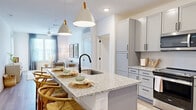 Located in Jacksonville, FL, this thoughtfully designed 2-bedroom, 2-bathroom residence offers a comfortable and modern living experience across a single floor. The open-concept kitchen and living area serves as the heart of the home, anchored by a granite-topped island with bar seating and pendant lighting. Grey shaker-style cabinetry, stainless steel appliances, and a matte black faucet complete the sleek kitchen aesthetic. Light wood-style flooring flows throughout the main living areas, enhancing the bright, airy ambiance. The living room is bathed in natural light from large windows dressed with sheer curtains, creating a welcoming and relaxed atmosphere. The primary bedroom is generously sized, featuring plush carpet, a ceiling fan, a bold accent wall, and a window with outdoor views. The second bedroom also offers ample space, vaulted-style ceilings, and access to a walk-in closet. Both bathrooms are finished with granite countertops, grey cabinetry, matte black fixtures, and glass-enclosed showers. A dedicated laundry room houses a full-size stacked washer and dryer with additional shelving. The entryway features a glass-paneled door that brings in natural light, offering a welcoming first impression to this well-rounded residence.