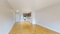 Located at 5600 Avenue Decelles in Montréal's Côte-des-Neiges–Notre-Dame-de-Grâce borough, this well-appointed one-bedroom, one-bathroom unit offers a comfortable and functional layout across a single floor. The living room is generously proportioned, bathed in natural light through large windows that frame views of the surrounding neighborhood. A skylight adds an additional source of brightness, and direct outdoor access through a side door enhances the sense of openness. The classic parquet flooring in a herringbone pattern runs throughout the living and bedroom areas, lending warmth and character to the space. The bedroom is notably spacious, offering ample room for furnishings, and features the same parquet flooring along with a window and baseboard heating. The kitchen has been updated with a modern aesthetic, showcasing two-tone cabinetry — crisp white lower units paired with textured wood-grain upper cabinets — complemented by light countertops, a subway tile backsplash, and large-format tile flooring. It is equipped with a full-size refrigerator, electric stove, built-in microwave, and dishwasher. The bathroom is clean and bright, finished with full white wall tiling and a soaking bathtub with chrome fixtures. Overall, the unit presents a bright, functional, and tastefully updated living space.