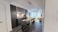 Located at Unit 808, 70 Ordnance Street in Toronto's dynamic King West neighbourhood, this well-appointed two-bedroom, one-bathroom suite offers a thoughtfully designed single-floor layout with generous overall floor area. The entrance leads into an open-concept living and kitchen zone finished with warm hardwood-style flooring throughout. The kitchen is sleek and contemporary, featuring dark wood-grain cabinetry extending to the ceiling with integrated under-cabinet lighting, a stone-finish waterfall island that doubles as a dining surface, stainless steel appliances, and a subway tile backsplash. The bright living room benefits from floor-to-ceiling windows dressed in sheer white curtains, allowing abundant natural light and views of the surrounding cityscape, with direct access to the private balcony. The primary bedroom is a serene retreat with large windows, sheer draping, and dark hardwood flooring, while the second bedroom is a compact, light-filled space with its own window. The bathroom features a dark wood-grain vanity with stone countertop, a large mirror with integrated shelving, and a separate full bathtub. A clean hallway with sliding storage connects the private spaces. The suite presents a cohesive modern aesthetic throughout with crisp white walls and quality finishes.