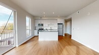 Located at 1501 NW 38th St in Kansas City, Missouri, this single-floor unit offers a clean, contemporary design with thoughtfully selected finishes throughout. The open-concept living and kitchen area serves as the heart of the space, showcasing warm-toned hardwood flooring, recessed lighting, and large windows that invite abundant natural light and views of the surrounding neighborhood. The kitchen is well-appointed with white flat-panel cabinetry, dark granite countertops, a subway tile backsplash, stainless steel appliances including a range, microwave, refrigerator, and dishwasher, and a central island that provides additional prep and counter space. The living area flows seamlessly from the kitchen, offering an open and versatile layout. A private balcony is accessible from the kitchen, extending the living space outdoors. The two bedrooms feature plush neutral carpeting and large windows with shade coverings, creating a calm and restful atmosphere. The primary bathroom includes a walk-in shower with white tile surround, a single-sink vanity with granite countertop, white cabinetry with matte black hardware, and hardwood-style flooring. A second full bathroom offers a tiled tub-shower combination and matching vanity finishes, maintaining design consistency throughout the unit.