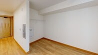 Located at 12370 SE Ash St in Portland, Oregon, this efficiently designed studio unit offers a thoughtful single-floor layout that maximizes functionality within a compact footprint. The open-plan living and kitchen area is unified by light wood laminate flooring and warm wood-toned baseboards, creating a cohesive and inviting atmosphere throughout.

The kitchen runs along one wall and is well-equipped with white cabinetry featuring modern bar-pull hardware, open shelving, a stainless steel sink, a white electric range, and a full-size white refrigerator. A ventilation hood is positioned above the range, and recessed lighting illuminates the space cleanly from above. The kitchen flows seamlessly into the main living area, which benefits from a window that brings in natural light.

A dedicated closet area with a built-in wire shelving rod provides practical storage, with an electrical panel neatly recessed into the wall nearby. The full bathroom is finished in neutral tones and includes a toilet, a single-sink vanity with a laminate countertop, and a shower/tub combo with a curtain rod and chrome fixtures. Grab bars are also present in the bathroom, adding a functional safety feature.

The entry door features a frosted glass panel, lending a clean, modern touch to the unit's straightforward and practical design.