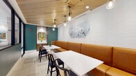 Located at 375 Summer Cypress Cove in Longwood, Florida, this single-floor community clubhouse offers a carefully curated blend of comfort and modern design. The space is divided into distinct yet interconnected areas, each thoughtfully finished to create a welcoming and functional environment.

The dining lounge features warm caramel leather banquette seating framed by natural wood paneling, set against a white painted brick accent wall adorned with a charming dog-themed mural. White square tables are paired with black rattan-accented chairs, while exposed Edison bulb pendant lights hang from a striking natural wood plank ceiling, adding warmth and character. A recessed display niche with a framed botanical artwork serves as a focal point along the teal accent wall.

Framed glass partitions with dark metal framing separate the lounge from the broader common area, maintaining visual connectivity while defining each zone. The main common area opens into a spacious game room featuring a full-size pool table as its centerpiece, bathed in natural light from large windows. Woven pendant fixtures illuminate the space, while organic sculptural wall décor and lush greenery add texture and life. The light tile flooring flows continuously throughout, unifying the entire space. A bar or kitchenette area is visible in the background, completing this well-appointed gathering space.