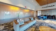 Located at 1600 Harbor Blvd in Weehawken, NJ, this impressively scaled amenity floor spans over 13,000 square feet and offers a thoughtfully curated collection of social and recreational spaces. The interior design is consistently sophisticated throughout, featuring bold abstract-patterned carpeting, warm wood wall paneling, and recessed lighting that create a modern yet inviting atmosphere.

The main lounge area makes an immediate impression with soaring double-height ceilings, a sleek linear fireplace framed by floor-to-ceiling wood paneling, and a dramatic pendant light fixture. Comfortable seating areas are arranged to encourage both relaxation and socializing. An adjacent lounge space features frosted glass partitions with glowing amber accents, offering a more intimate setting alongside a dining nook outfitted with vibrant blue chairs and large windows that flood the area with natural light.

A dedicated game room houses dual billiard tables, leather lounge chairs, and sculptural artwork, while high-top seating areas with views to the outdoors add a lively, social dimension to the space.

Outside, a beautifully maintained courtyard and terrace walkway weave between the residential buildings, lined with ornamental grasses, manicured hedges, and stone-paved paths. The outdoor spaces offer stunning, unobstructed views of the Manhattan skyline, making this a truly exceptional urban amenity destination.