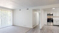 This single-floor residence offers a clean, modern aesthetic throughout its thoughtfully designed layout. The open living area features a combination of luxury vinyl plank flooring and plush carpeting, with large vertical-blind-covered sliding doors that invite natural light and provide access to the outdoors. A textured ceiling adds subtle character to the space.

The kitchen is a functional highlight, outfitted with crisp white shaker cabinetry, a classic white subway tile backsplash, light quartz countertops, a stainless steel sink, and a full suite of stainless steel appliances including a range, over-the-range microwave, and refrigerator. A ceiling fan overhead adds comfort to this well-lit culinary space.

The bedrooms are carpeted for comfort, each featuring ample natural light from windows with blinds. One bedroom includes floor-to-ceiling mirrored sliding closet doors, while another features a ceiling fan and an additional closet. Both rooms maintain a bright, neutral palette.

The bathroom is finished with large-format stone-look tile on both the floors and the full tub surround, complemented by a white soaking tub, a white vanity with an integrated sink, and brushed nickel hardware throughout. The overall ambiance of the residence is clean, neutral, and move-in ready.